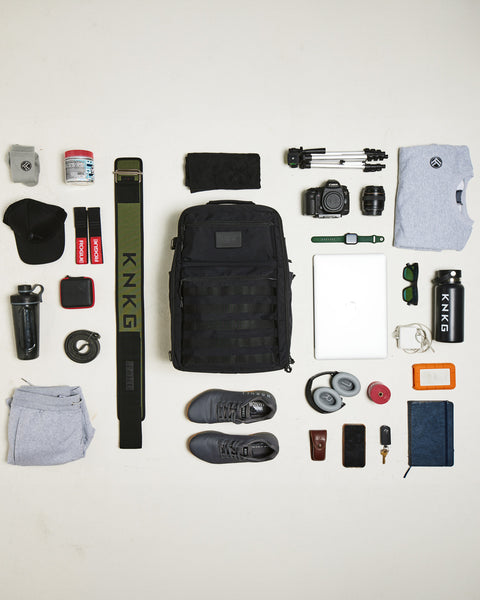 Flat lay of gym items that fit inside the large black CONQUER Backpack