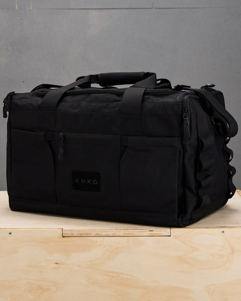 Front view of large black KNKG CORE Duffel sitting on wooden box