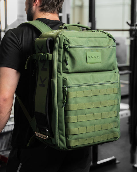 Man in gym wearing large green CONQUER Backpack