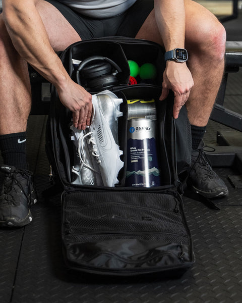 Internal dividers of large black CONQUER Backpack packed with shoes, protein, headphones and various workout accessories