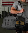 Man wearing black CORE Duffel over shoulder in gym, with American Flag in background