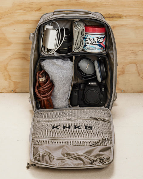Internal view of neutral beige KNKG CONQUER backpack dividers packed with GHOST preworkout, leather skipping rope, headphones and camera gear