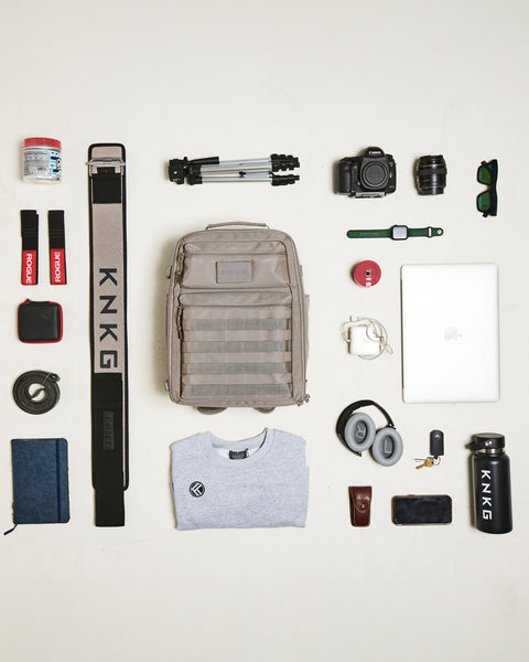 Flat lay of gym items being packed in neutral beige KNKG CONQUER backpack