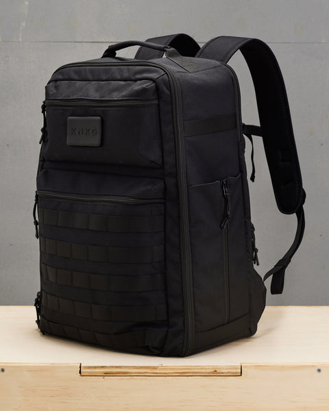 Side view of large black CONQUER Backpack sitting on wooden box