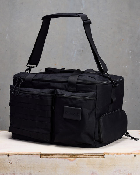 black CONQUER Duffel sitting on wooden box with shoulder strap suspended