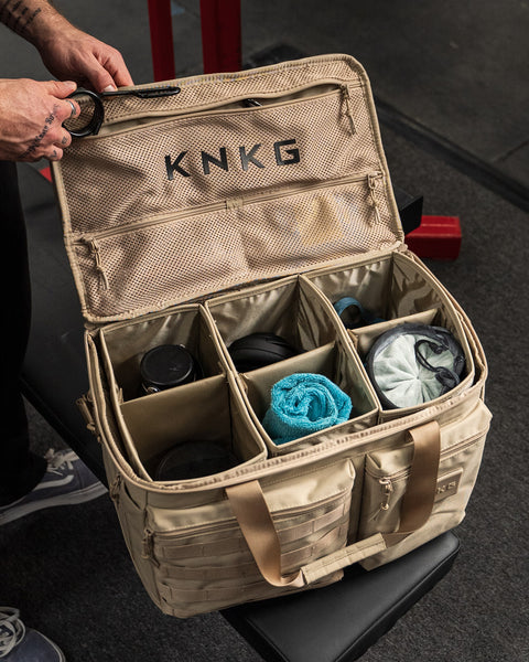 Person unpacking neutral beige KNKG CONQUER Duffel inside gym