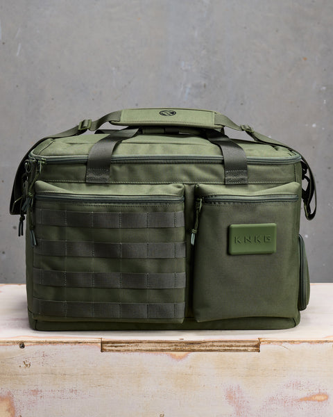 Front view of Green KNKG CONQUER Duffel  sitting on wooden box