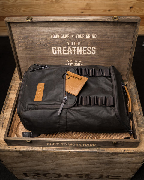 KNKG Waxed Canvas Backpack with leather wallet sitting inside wooden box packaging.