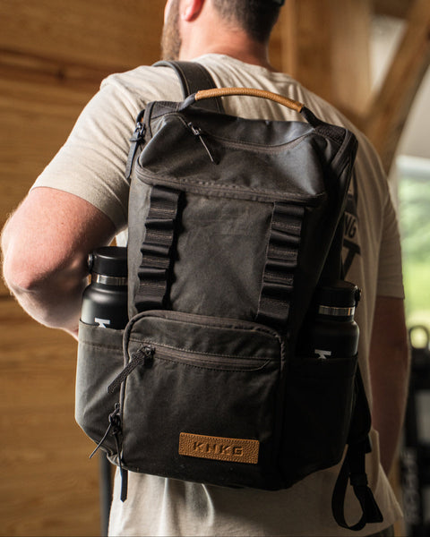 Man wearing KNKG Waxed Canvas Backpack in barn gym