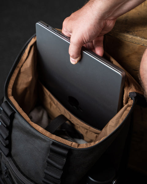 Person placing a laptop into KNKG Waxed Canvas Backpack
