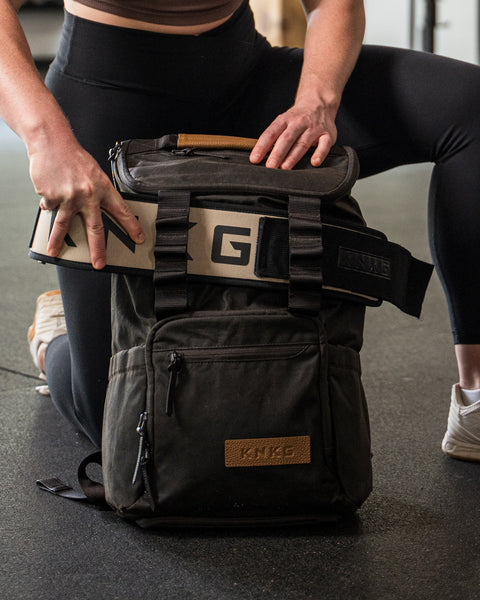 Person removing weight lifting belt from KNKG Waxed Canvas Backpack lifting belt sleeve.