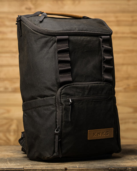 KNKG Waxed Canvas Backpack side view sitting on wooden box inside barn gym
