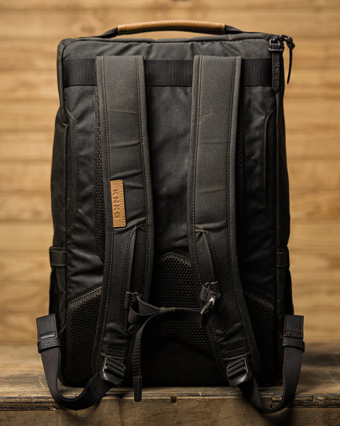Back view of KNKG Waxed Canvas Backpack showing leather logo