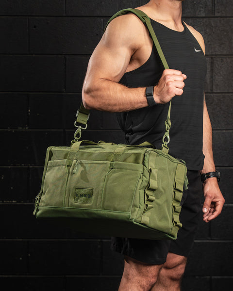 Man wearing green CORE Duffel over shoulder, standing in front of black brick wall