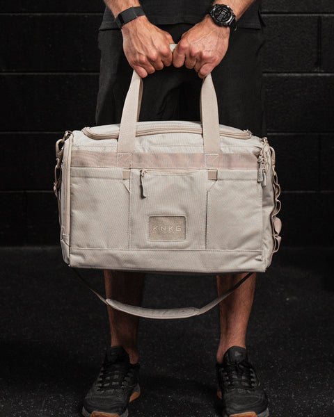 Man holding beige neutral CORE Duffel by grab handle