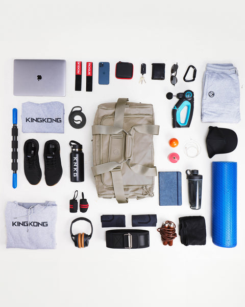 Flay lay of large neutral beige CORE Duffel surrounded by gym gear that fits inside bag