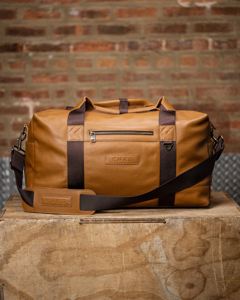 large tan HERITAGE leather duffel sitting on wooden box