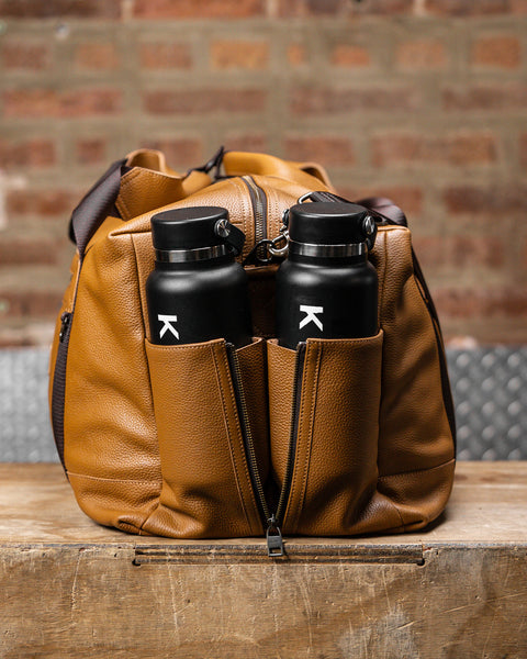 Two drink bottles packed inside large tan HERITAGE leather duffel pockets