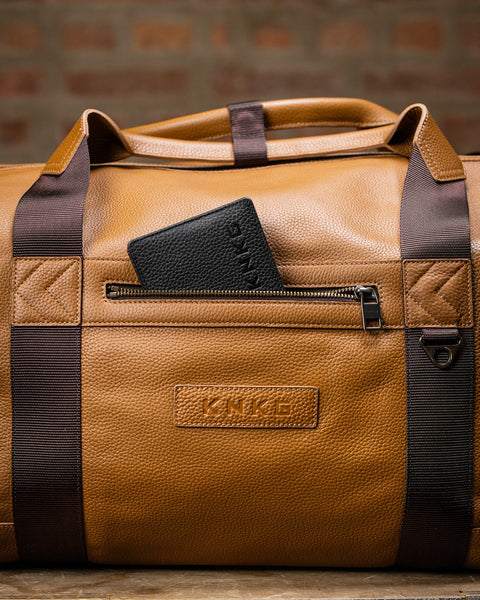Close up of black wallet inside large tan HERITAGE leather duffel zippered pocket