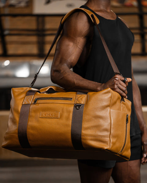 Man wearing large tan HERITAGE leather duffel over shoulder inside boxing gym