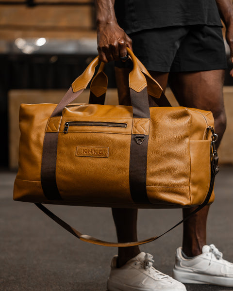 Person holding large tan HERITAGE leather duffel