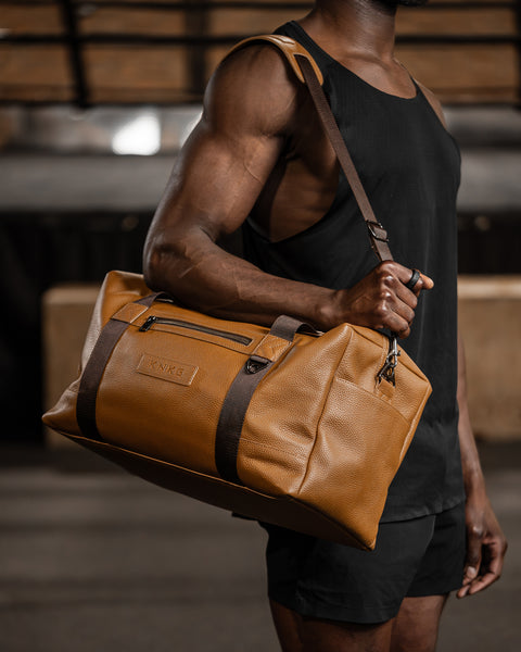 Man carrying tan HERITAGE leather duffel over shoulder inside boxing gym