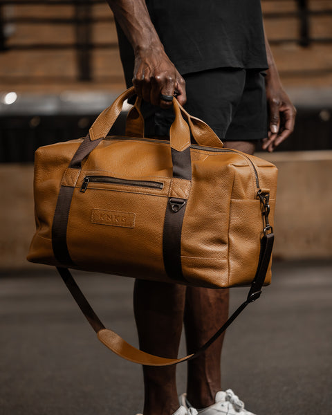 Man carrying tan HERITAGE leather duffel inside gym