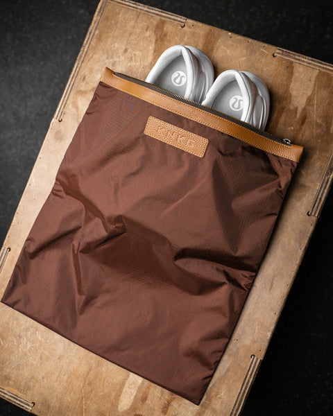 Lululemon sneakers packed inside brown shoe bag with leather KNKG logo, sitting on wooden box