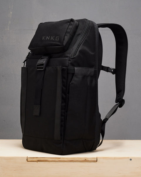 Side view of Black KNKG PLUS Backpack sitting on wooden box