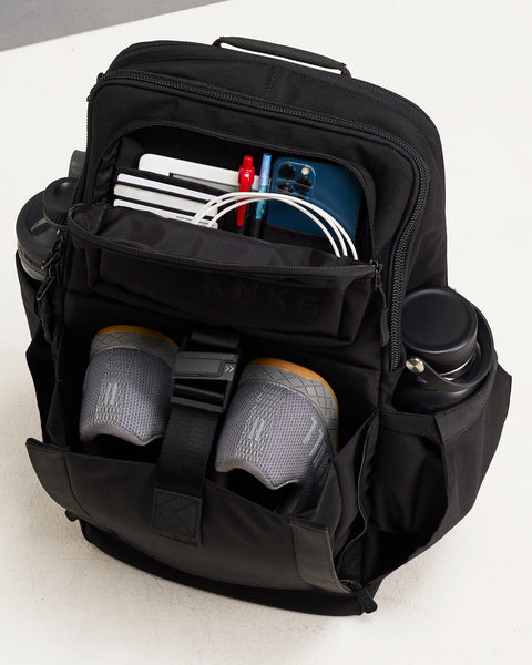 Internal view of Black KNKG PLUS Backpack packed with shoes, water bottles, phone, charger and EDC essentials