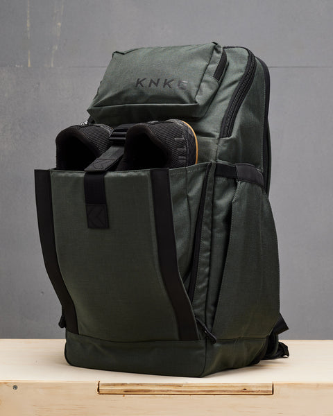 charcoal KNKG PLUS Backpack with shoes inside front pocket, sitting on wooden box