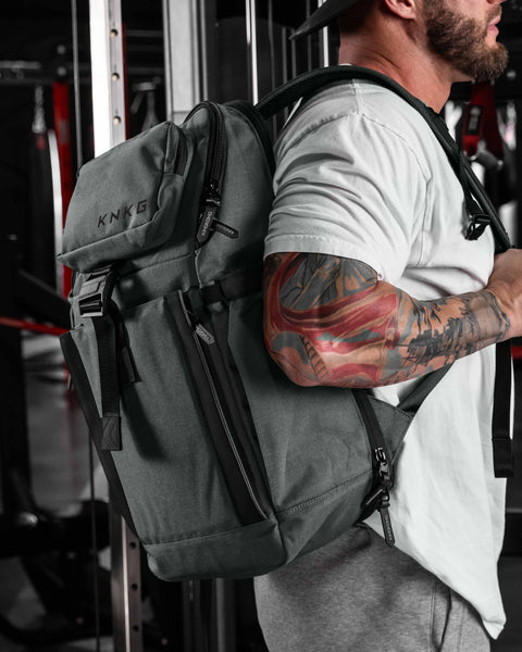 Man wearing charcoal KNKG PLUS Backpack over shoulder inside gym