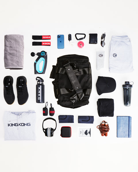 Flat lay of small black KNKG PLUS Duffel bag sitting on floor surrounded by gym gear