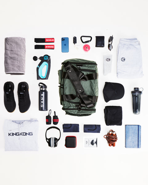 Flat lay of charcoal grey KNKG PLUS duffel bag sitting on ground surrounded by gym gear