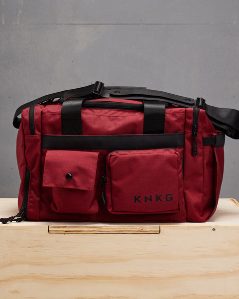 small red KNKG PLUS Duffel  sitting on wooden box