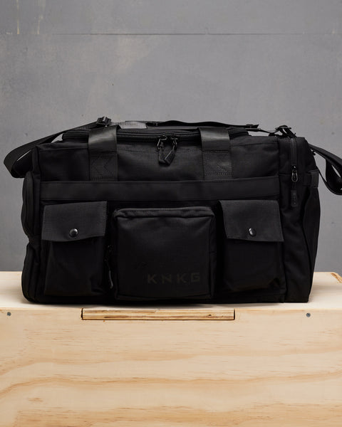 Front view large black KNKG PLUS duffel bag  sitting on wooden box