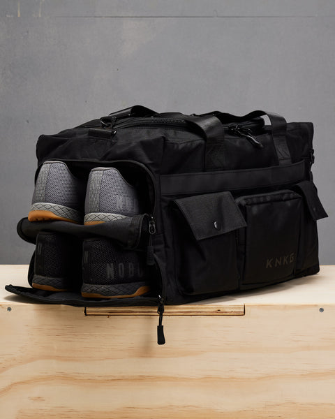 Two pairs of NOBULL sneakers packed inside black KNKG PLUS duffel bag