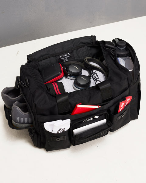 Birds eye view of sneakers, hoodie, headphones, bottles, notebook and mobility accessories packed inside large black KNKG PLUS duffel bag