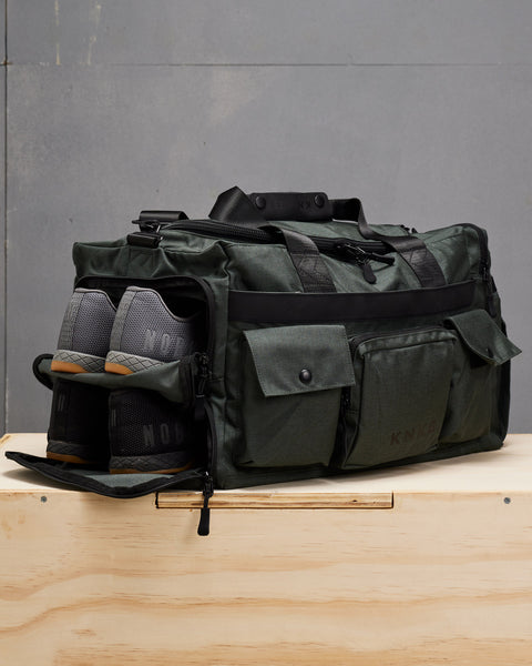 Two pairs of NOBULL sneakers packed inside charcoal grey PLUS Duffel  shoe compartments
