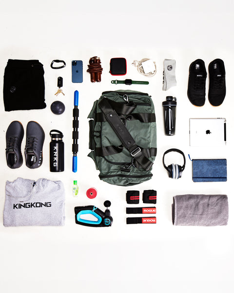 Flat lay of charcoal grey KNKG PLUS Duffel bag sitting on ground surrounded by workout gear