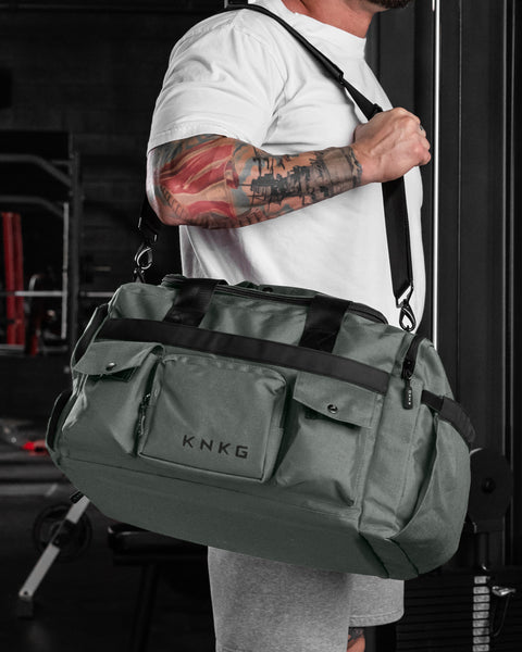 Man wearing charcoal grey KNKG PLUS Duffel bag over shoulder in gym