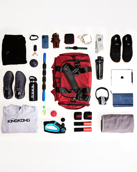 Flat lay of gym essentials being packed in medium red KNKG PLUS Duffel
