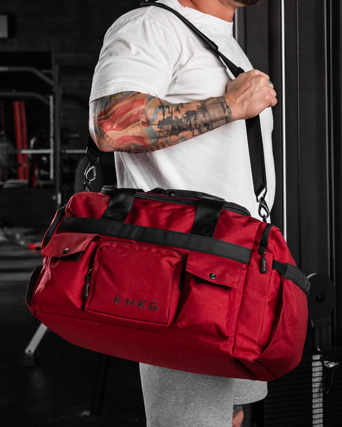 Bodybuilder carrying red KNKG PLUS Duffel in gym