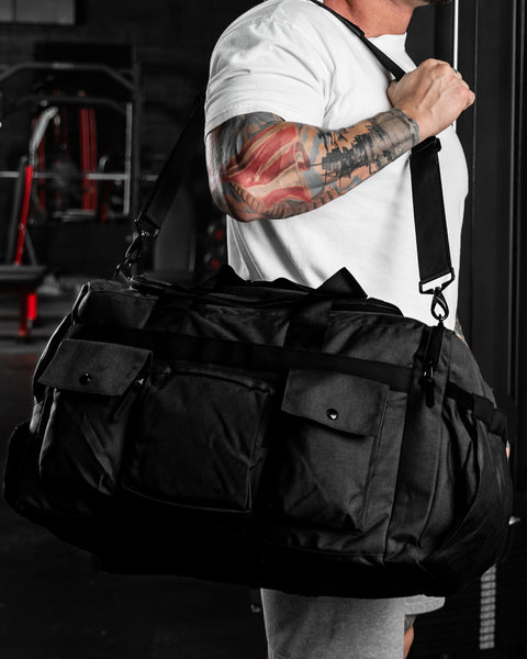 Weightlifter in gym carrying large black KNKG PLUS duffel over shoulder