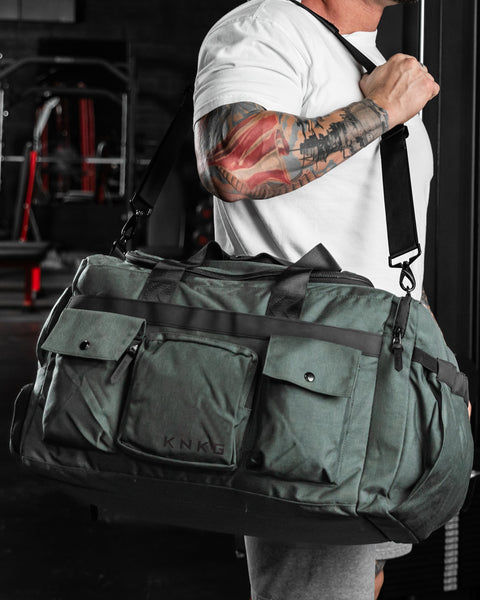Bodybuilder carrying KNKG large charcoal PLUS Duffel over shoulder