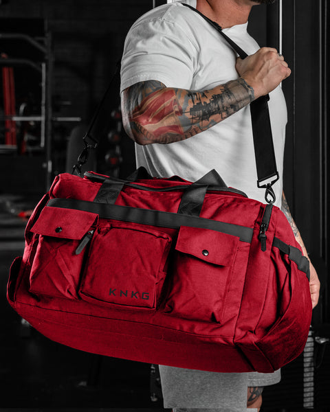 Person carrying KNKG large red PLUS Duffel over shoulder