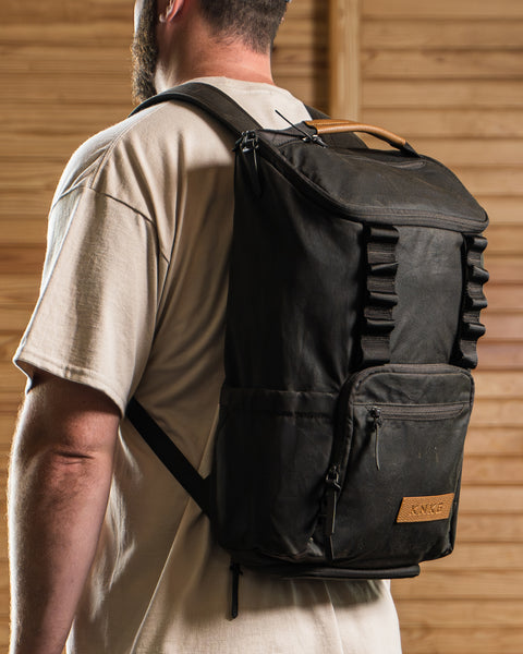 Man wearing KNKG Waxed Canvas Backpack in front of wooden background