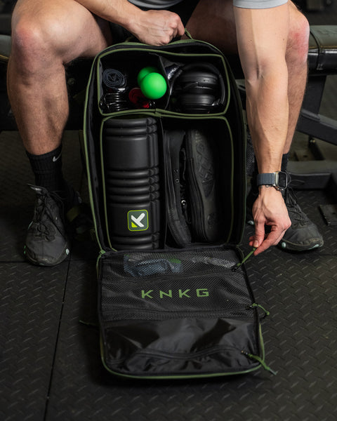 Internal dividers of large green CONQUER Backpack paced with foam roller, sneakers, headphones and workout accessories
