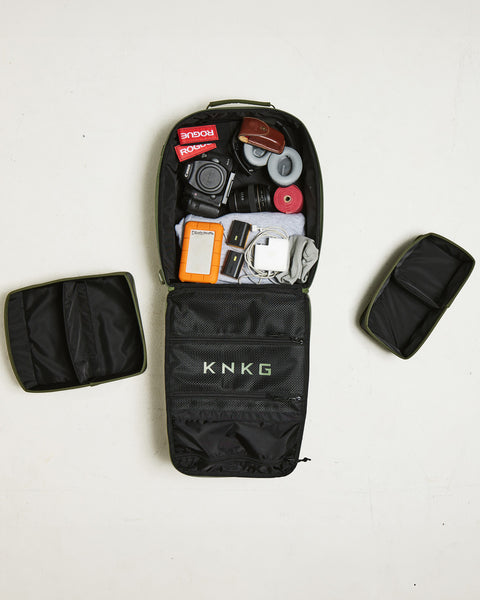 Birds eye view of small green KNKG CONQUER Backpack packed with camera, hoodie, headphones and mobility accessories