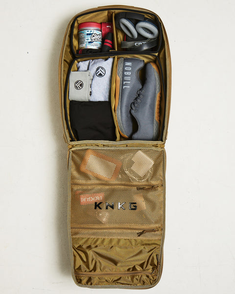 Flat lay of internal dividers inside desert KNKG CONQUER Backpack packed with shoes, pre-workout, headphones, wrist wraps, socks and spare clothes